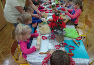 Dzieci przy ozdobionym świątecznie stole rozwałkowują ciasto na pierniki.